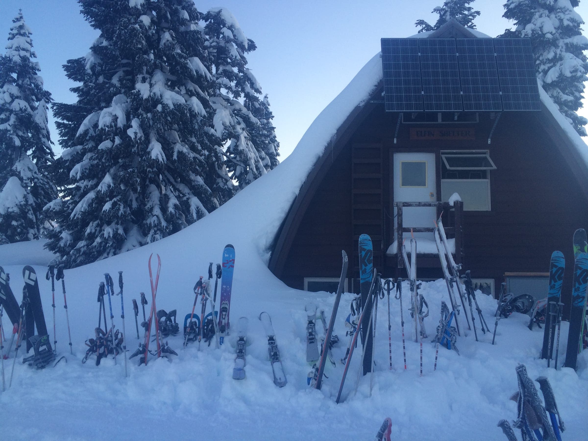 Touring skis and snowshoes stand in the snowbank outside the Elfin Lakes Shelter in winter.
