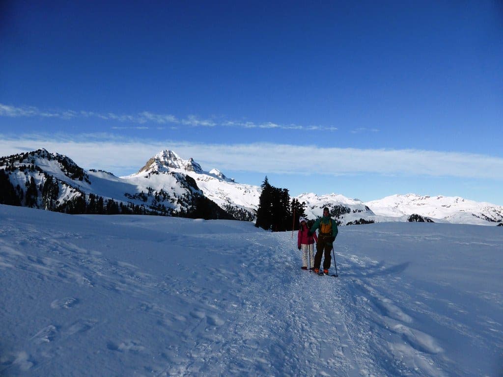 Two snowshoers cross open snow on the Elfin Lakes route with Garibaldi Park peaks ahead.