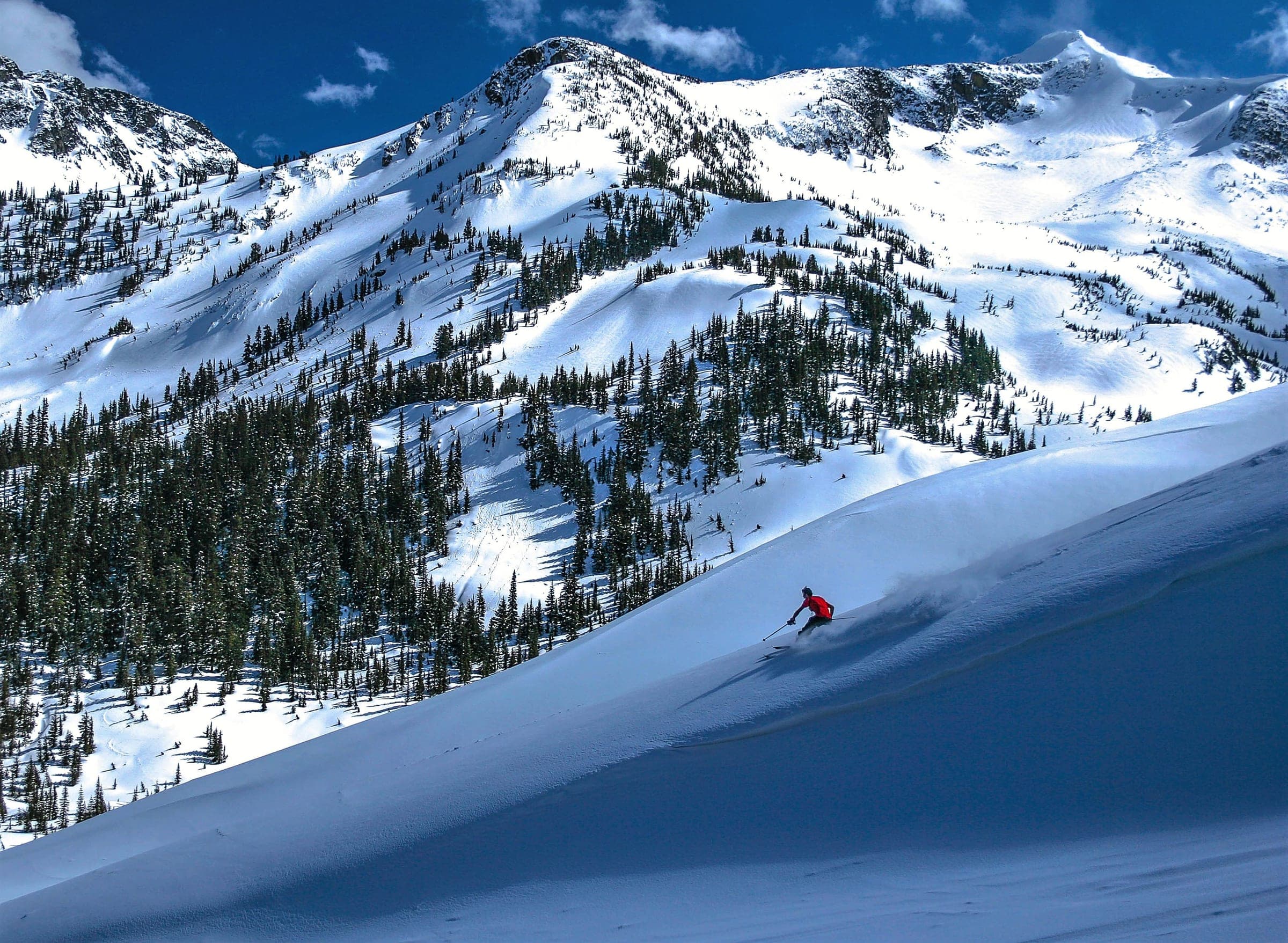 A skier carves fresh snow near Keith's Hut with Vantage Peak and the Joffre Group behind.