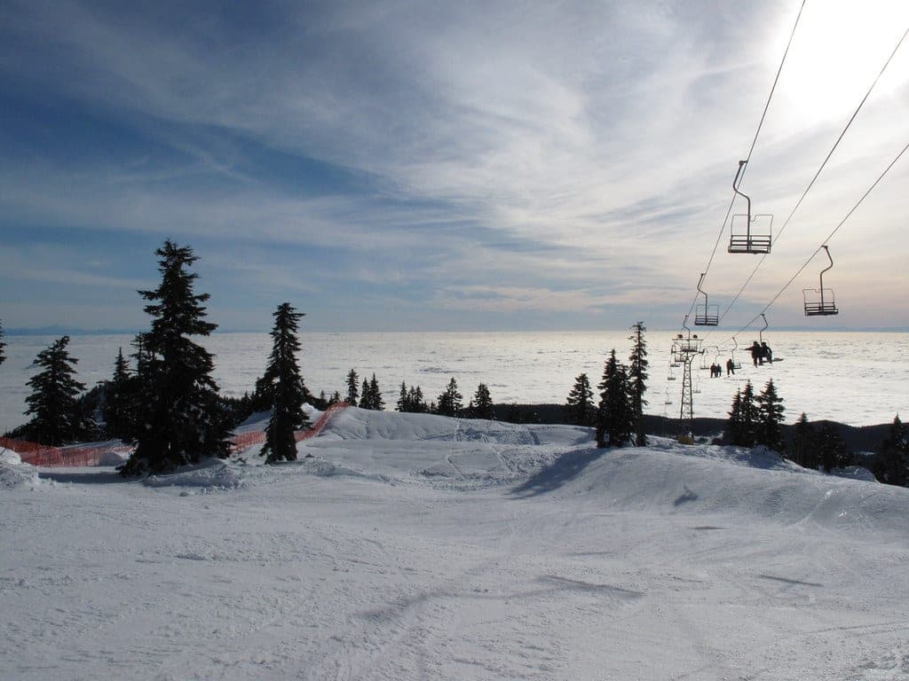 A chairlift climbs Mount Strachan's snowy slopes above a cloud inversion that hides the city below.