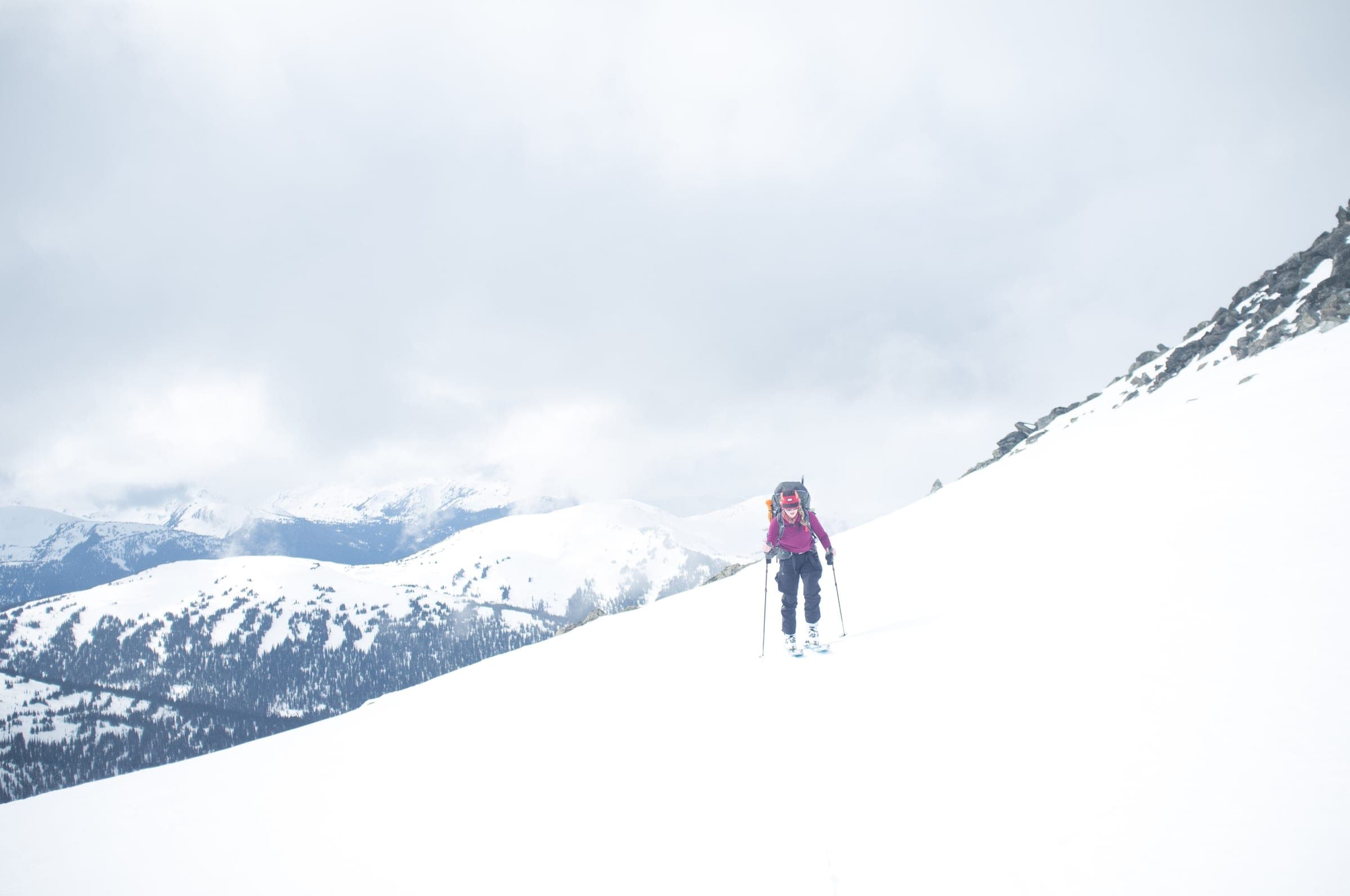 A ski tourer skins up a broad snow slope on the Spearhead with the Coast Mountains behind.