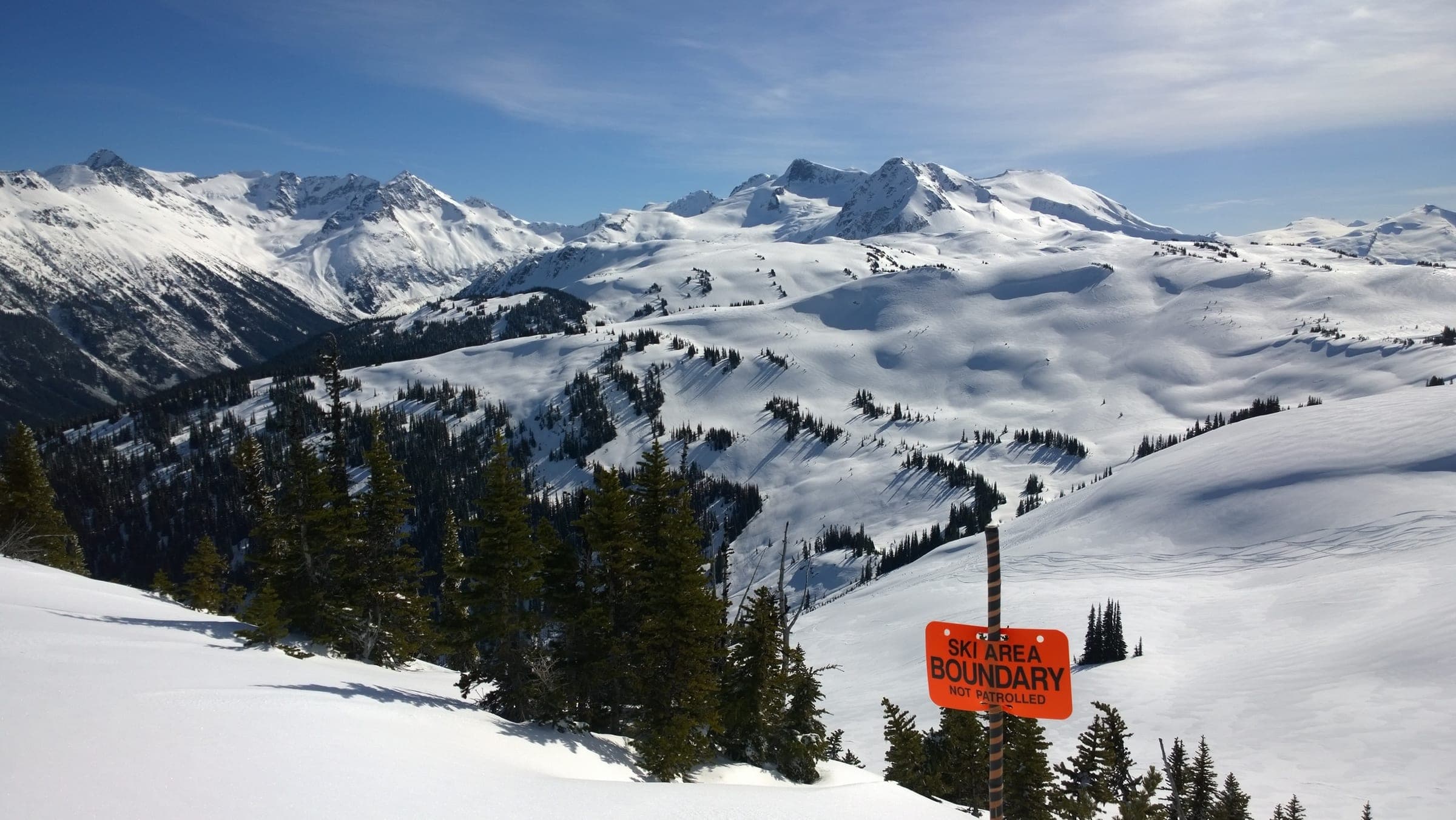 A ski area boundary sign marks the edge of Whistler Blackcomb above open backcountry bowls and peaks.