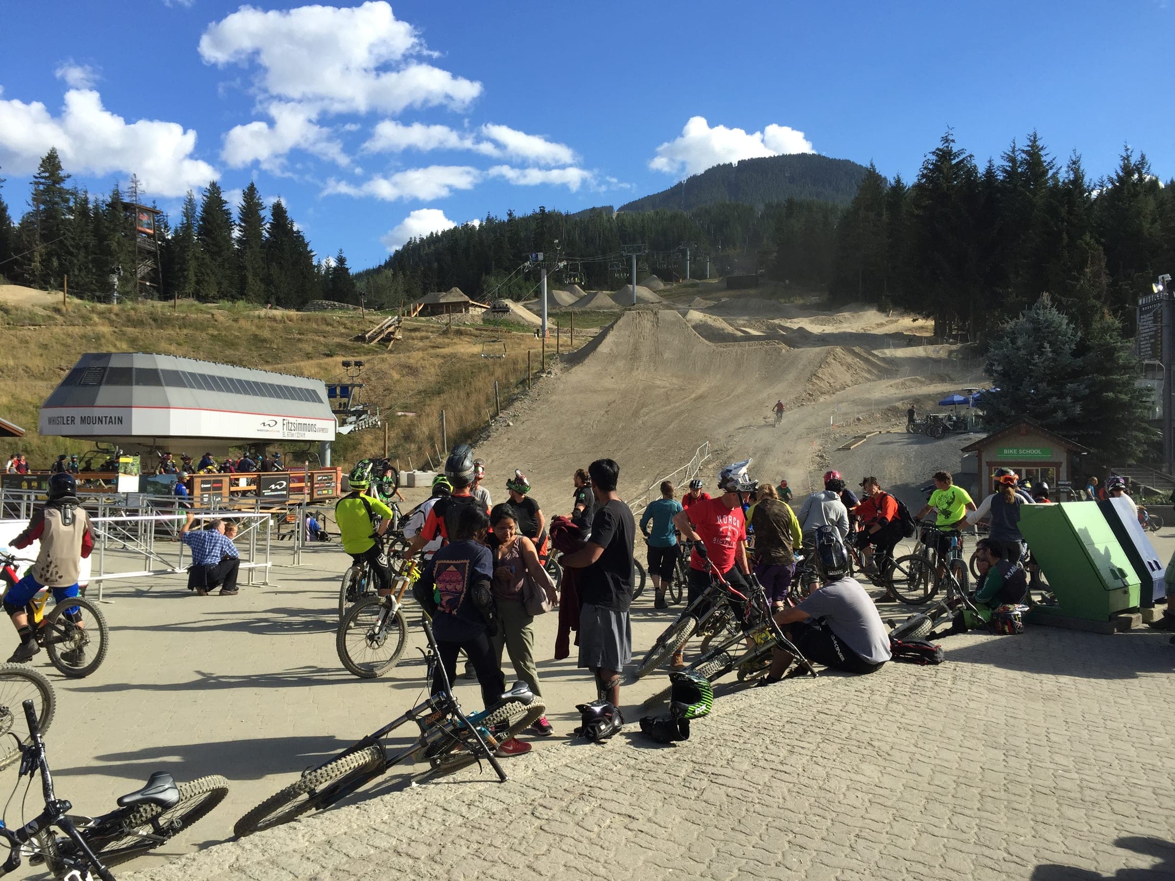 Riders gather with their bikes at the base of Whistler Mountain below the dirt lines of the bike park.