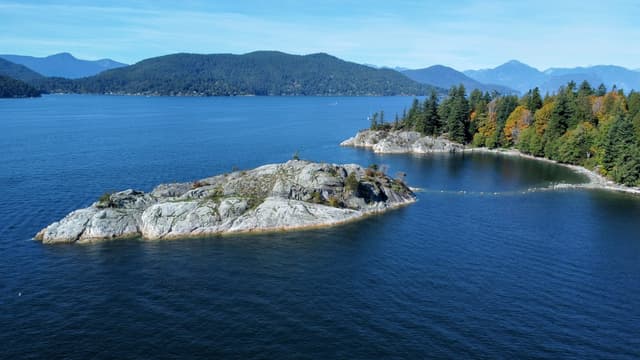 Whytecliff Islet sits off the forested point of Whytecliff Park with Howe Sound and its mountains behind.