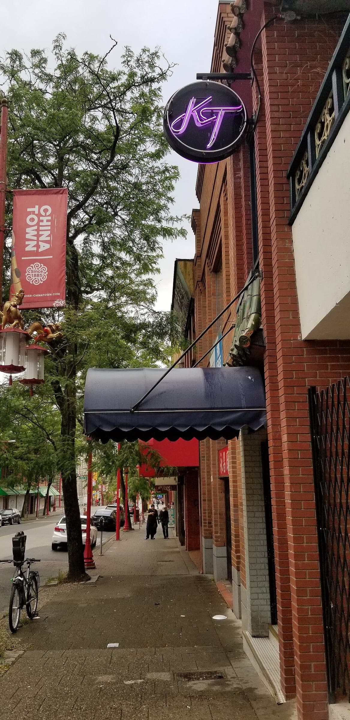 Kissa Tanto's neon KT sign hangs over a navy awning on a brick block in Vancouver's Chinatown.