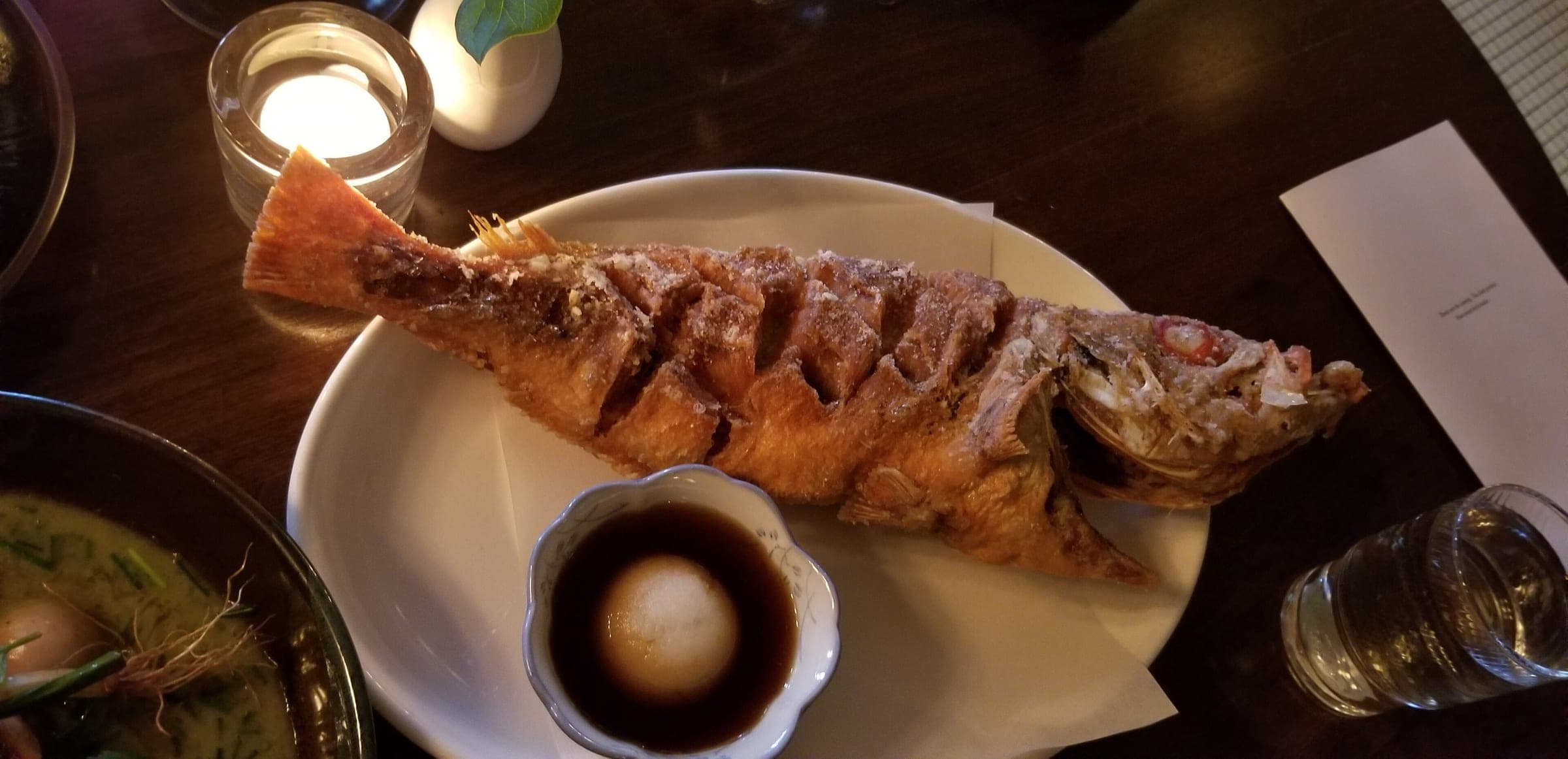 A fried whole fish with a dipping sauce on a candlelit table at Kissa Tanto in Chinatown.