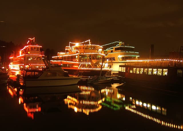 Carol ships strung with Christmas lights double in the still water of Coal Harbour in December.
