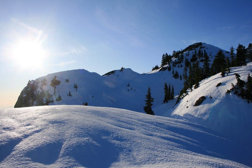 Sun flares over the snow-covered ridge of Mount Seymour under a deep blue sky