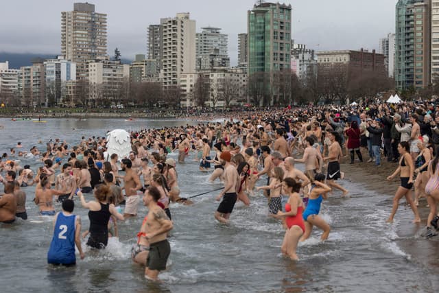 Hundreds of swimmers splash into English Bay below the West End towers at the 2025 Polar Bear Swim.