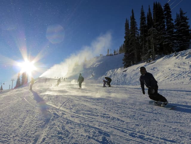 Snowboarders carve down a groomed run past snow guns into low sun on Whistler's opening day in November 2013.