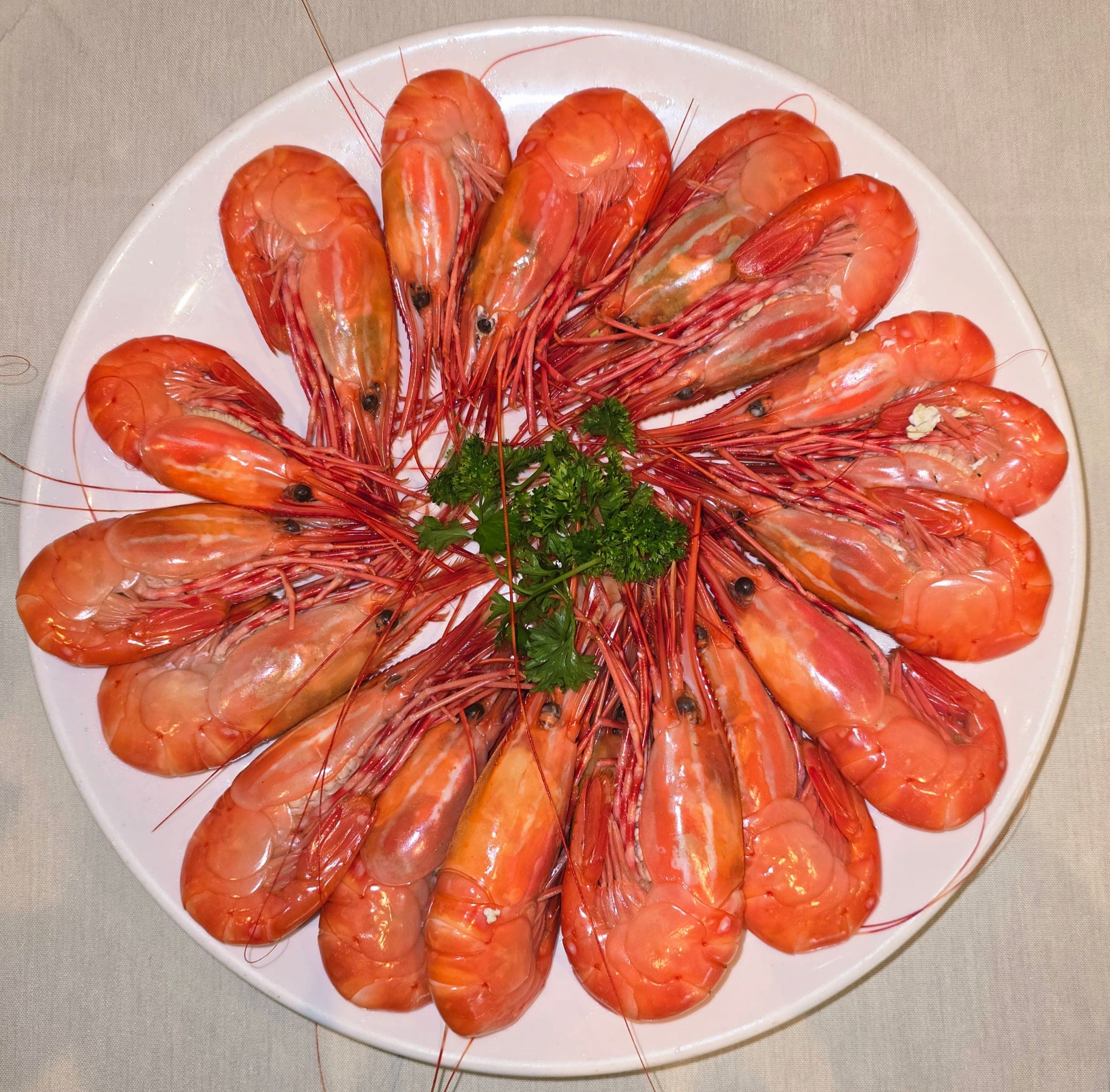Steamed spot prawns fan out in a ring around a sprig of parsley on a white platter.