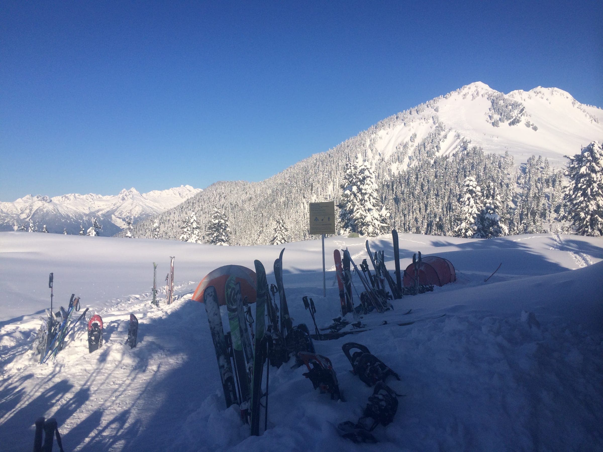 Skis and snowshoes stand in the snow outside the Elfin Lakes hut on a clear March morning.