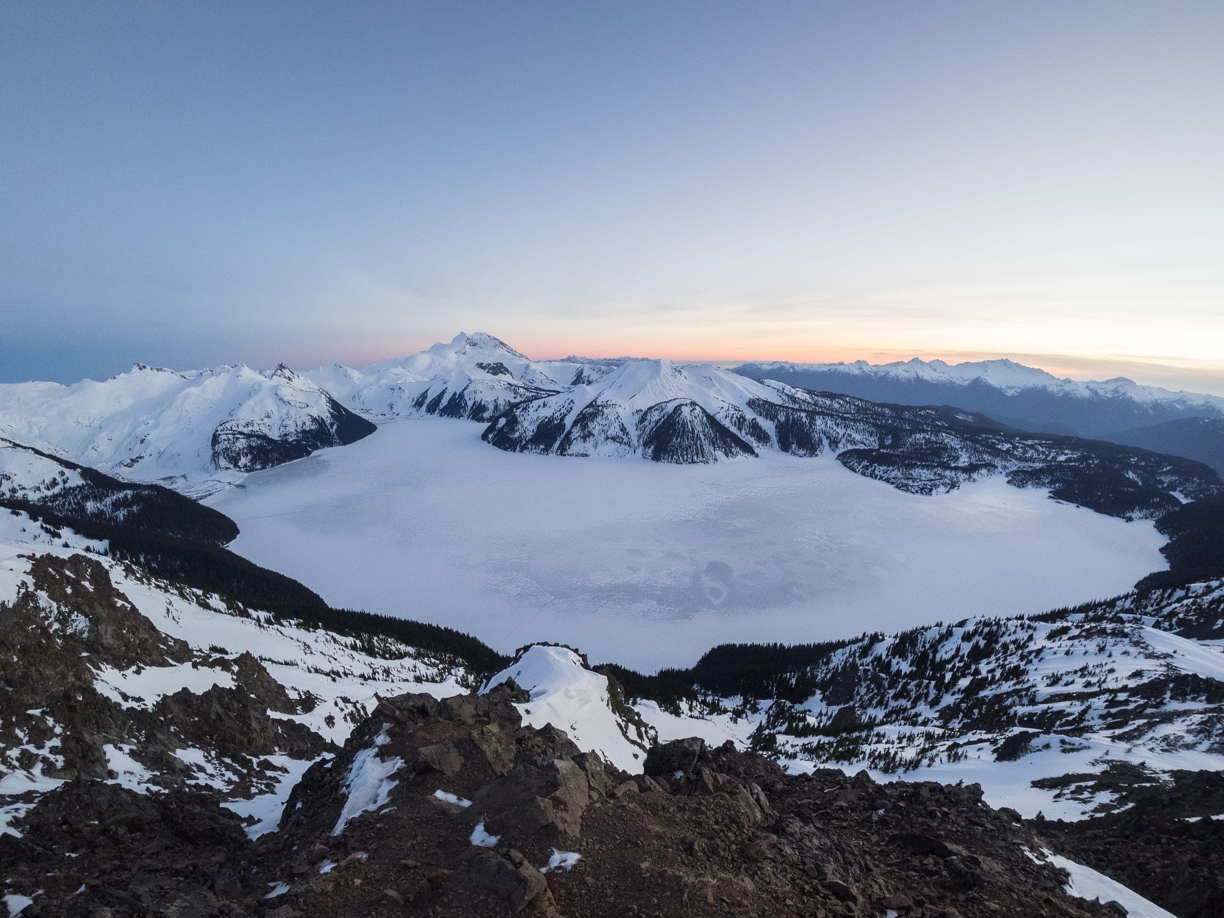 Frozen Garibaldi Lake lies white below snowy peaks in the winter view from the top of Panorama Ridge.