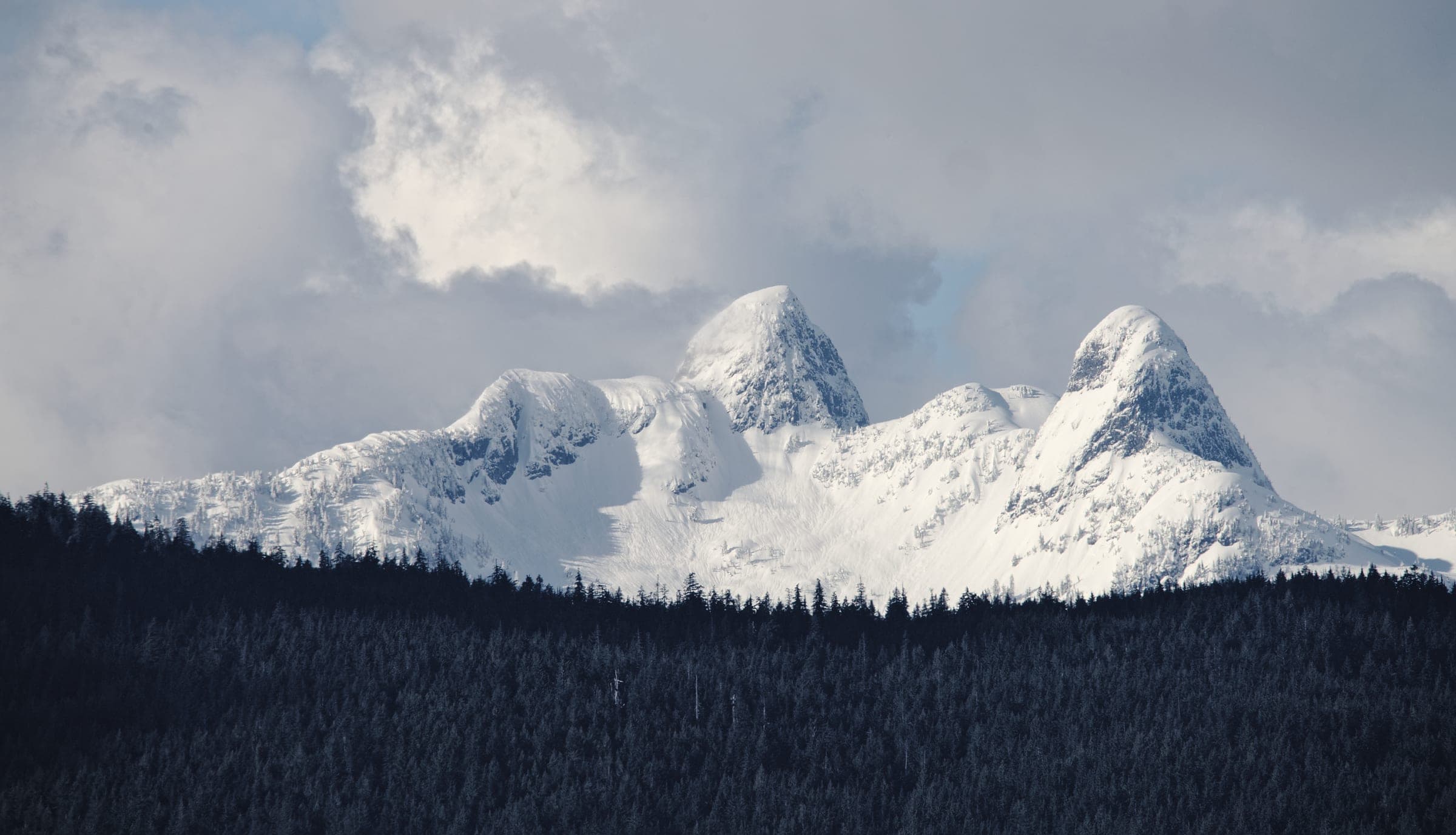 Fresh snow covers the twin granite peaks of the Lions above a dark band of North Shore forest.