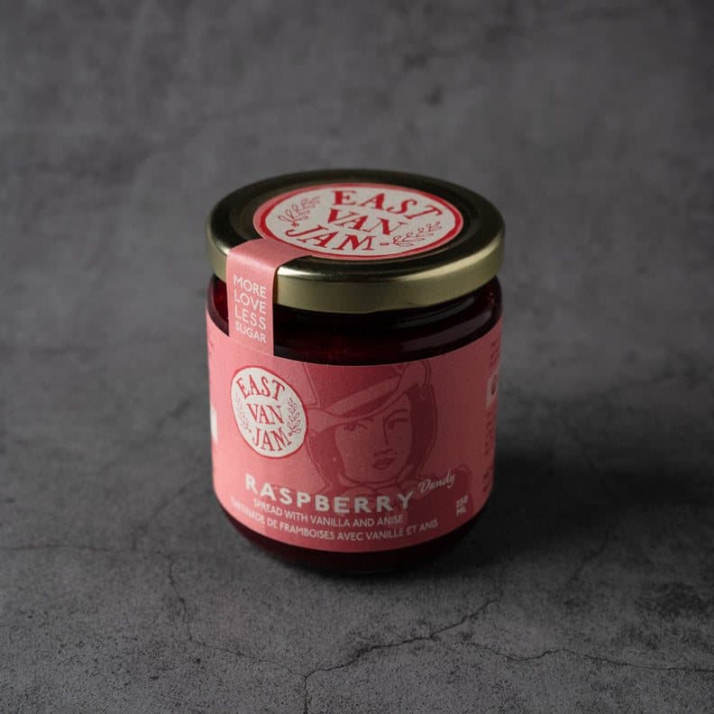A jar of East Van Jam raspberry spread on a grey stone surface.