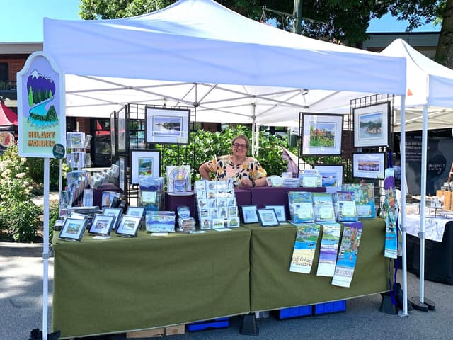 Hilary Morris at her market tent, with framed prints, calendars and cards set out on the table.