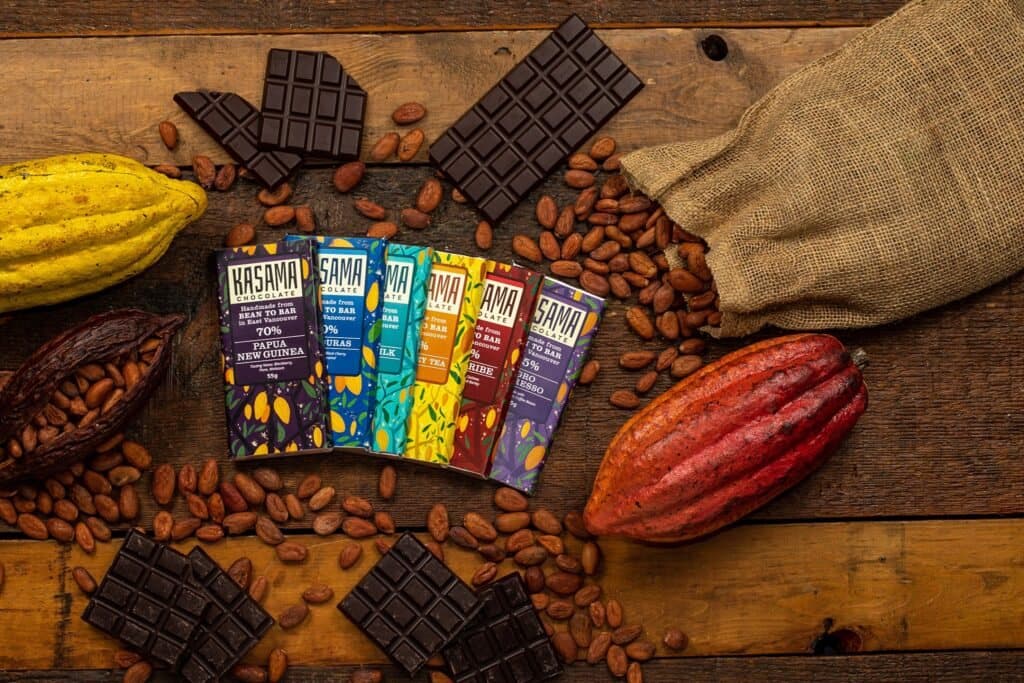 Kasama Chocolate bars laid out among cacao pods, cacao beans and broken squares of chocolate on a wooden board.