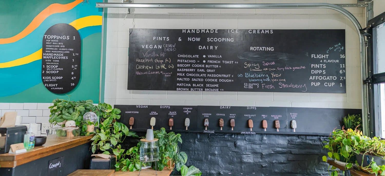 The counter at Melt Confectionary under a chalkboard menu of ice cream flavours and a bright painted wall.
