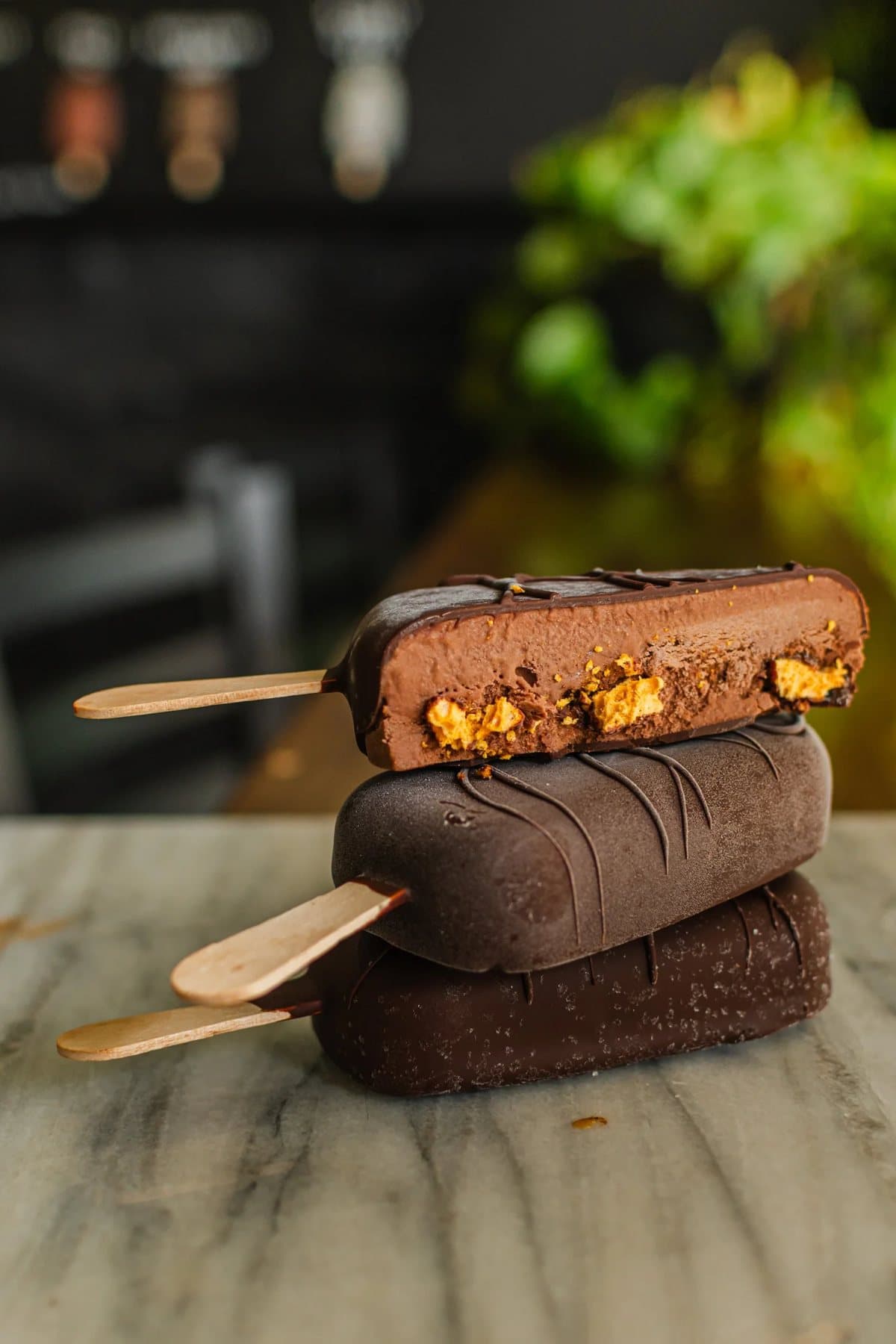 Three chocolate-dipped ice cream bars from Melt Confectionary stacked on a marble counter.