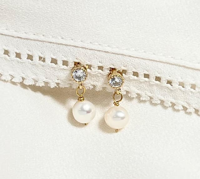 Reminded Designs pearl drop earrings with crystal studs pinned to white lace.
