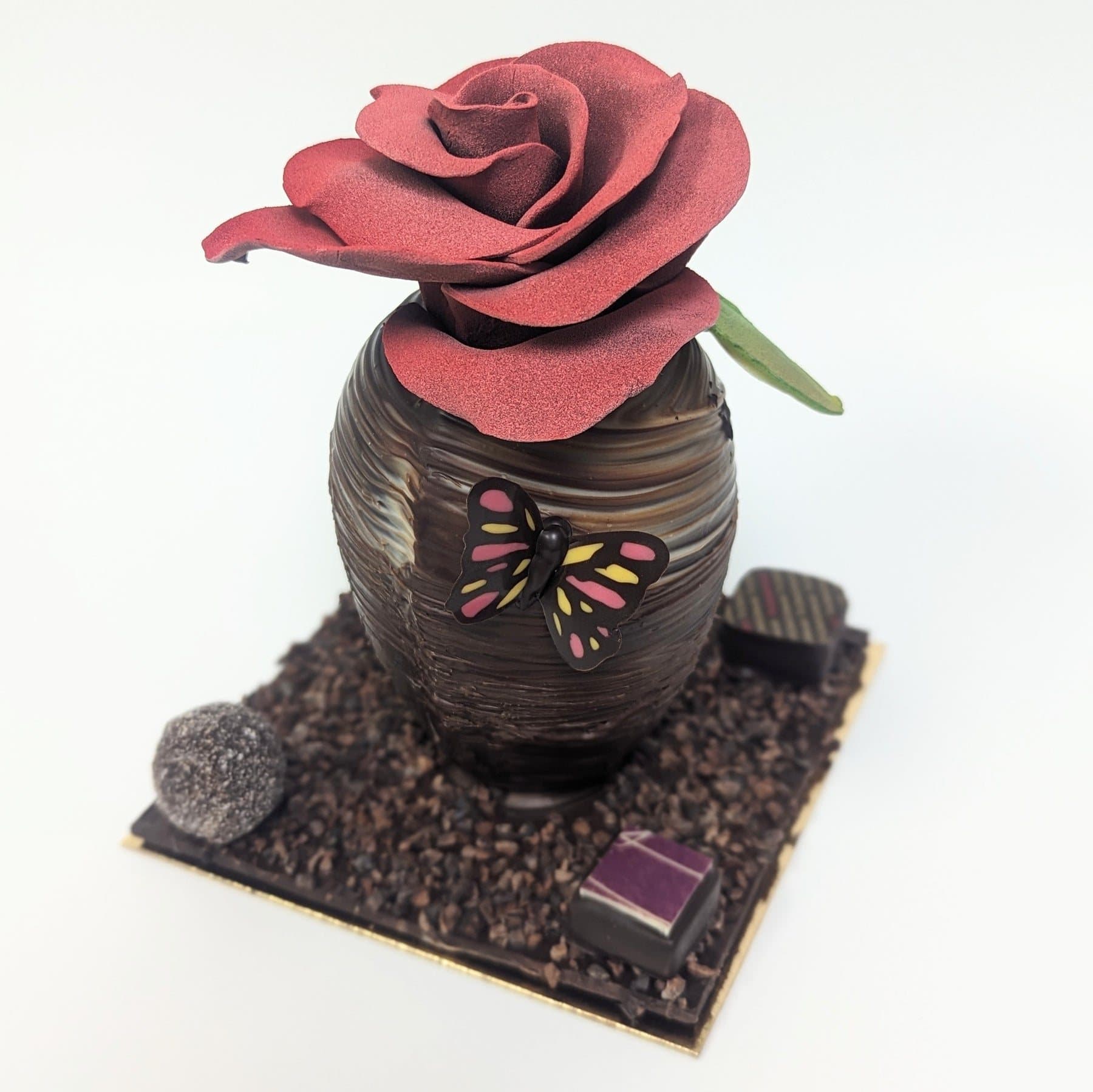 A Thomas Haas chocolate flowerpot painted with a butterfly and topped with a red chocolate rose.