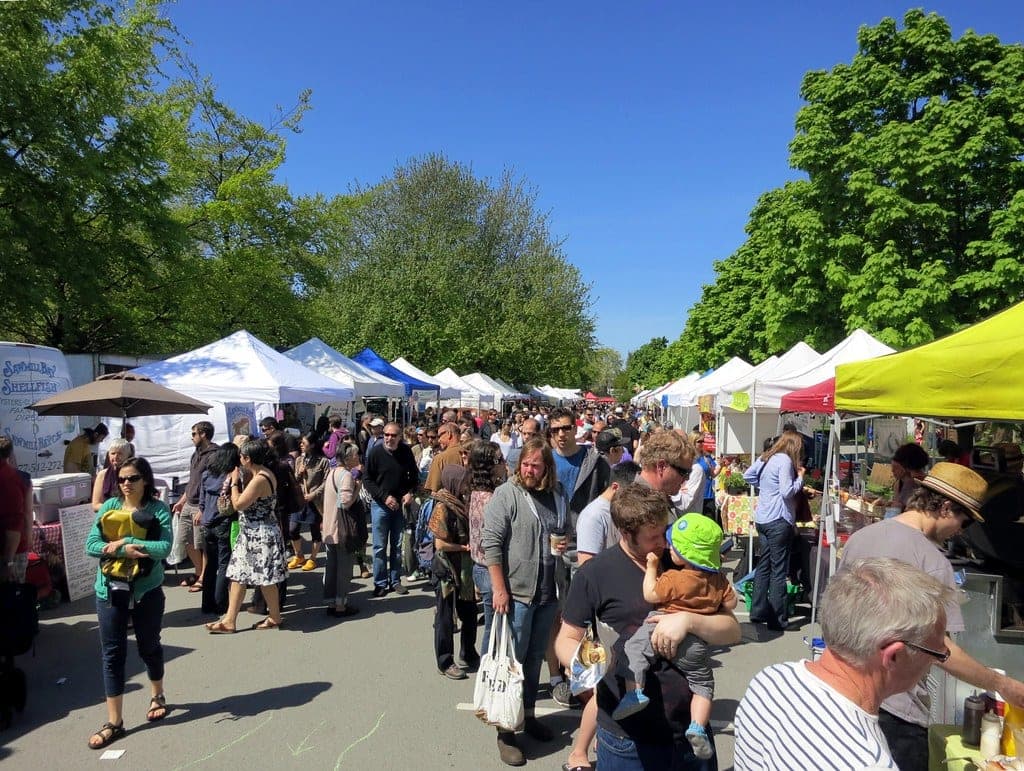 Crowds browse rows of white tents at the Trout Lake Farmers Market on a sunny Saturday