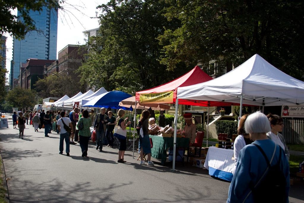 Stalls line the street at the West End Farmers Market with downtown towers behind
