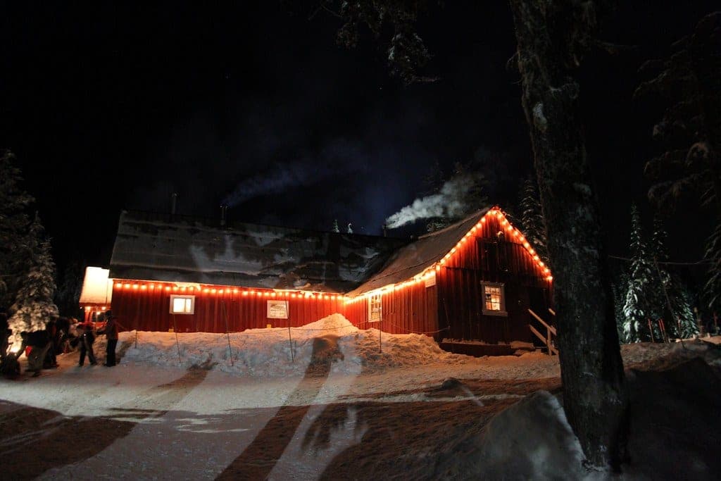 String lights outline Hollyburn Lodge on a winter night as woodsmoke rises from its chimney.