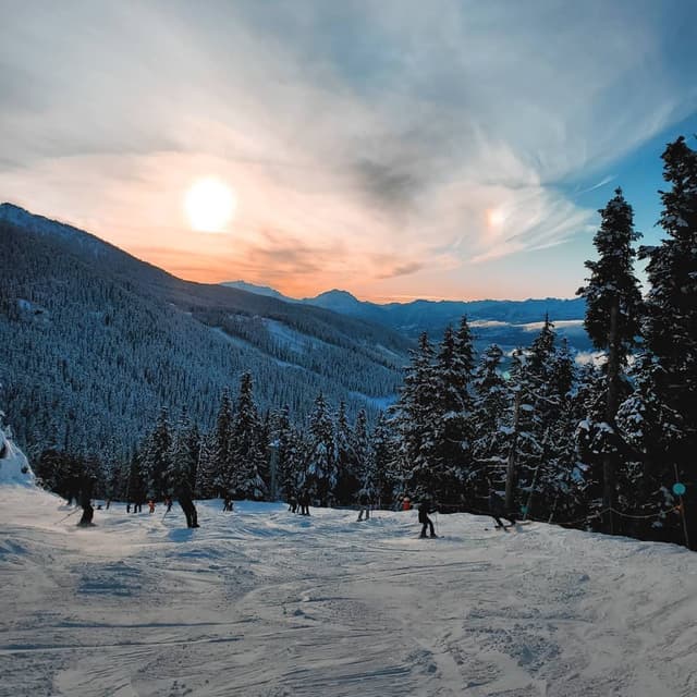 Skiers on a groomed Whistler run at sunset, from Black Tie Skis of Whistler.