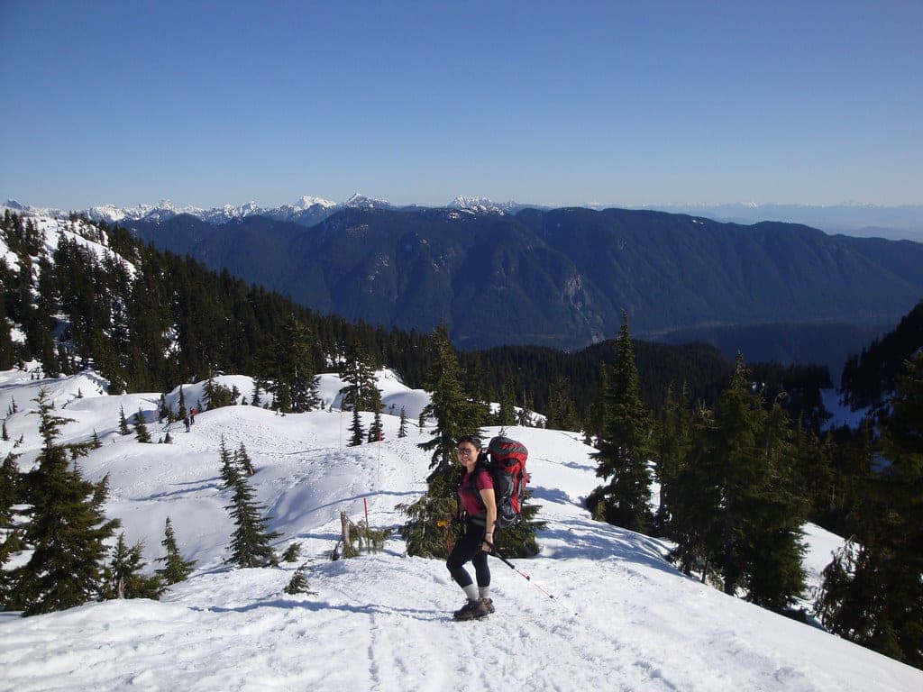 A snowshoer climbs a sunny snow slope on Mount Seymour with the Coast Mountains behind.