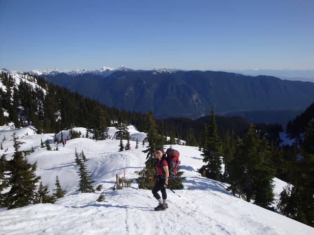 A snowshoer climbs a sunny snow slope on Mount Seymour with the Coast Mountains behind.