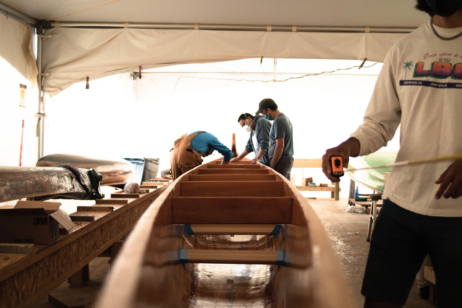 People work on a wooden canoe hull inside the Canoe Cultures building workshop.