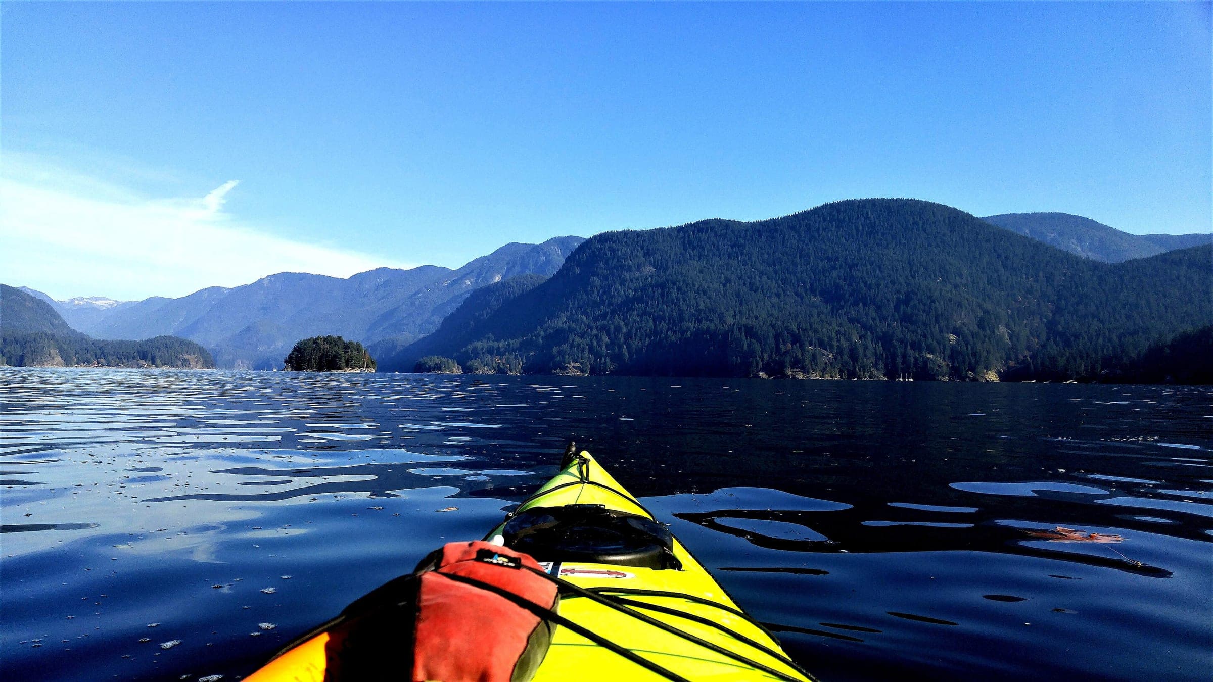 A yellow kayak bow points down Indian Arm from Deep Cove toward forested mountains.