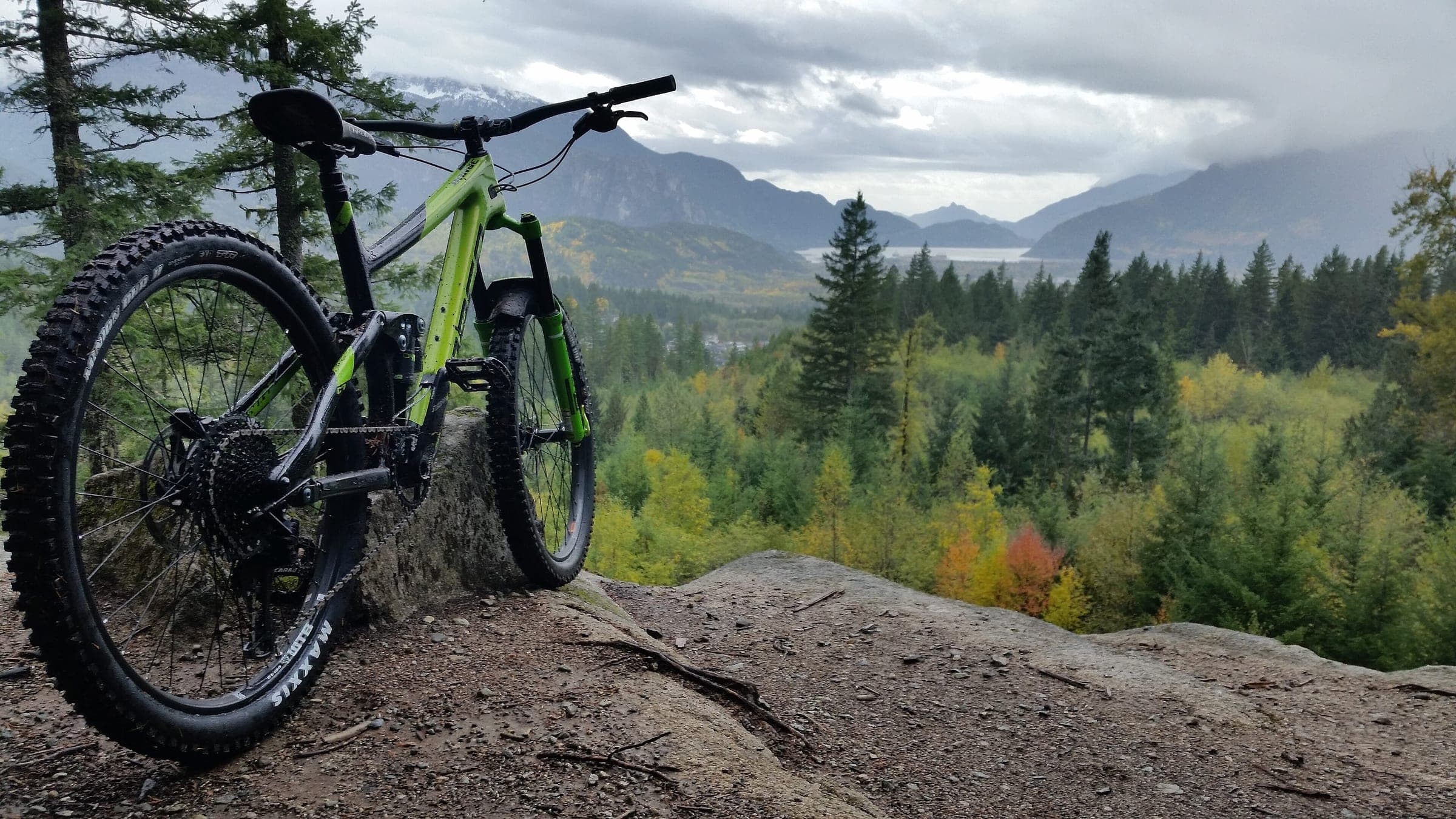 A full-suspension mountain bike rests on a rock above Squamish with the valley and mountains behind.