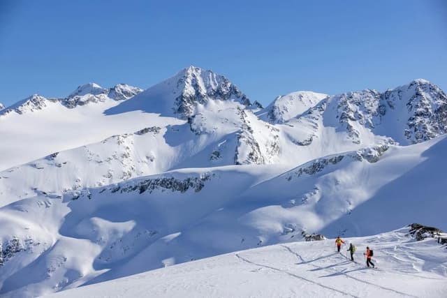A small group of skiers crosses a snowy bowl below peaks on an Extremely Canadian trip.