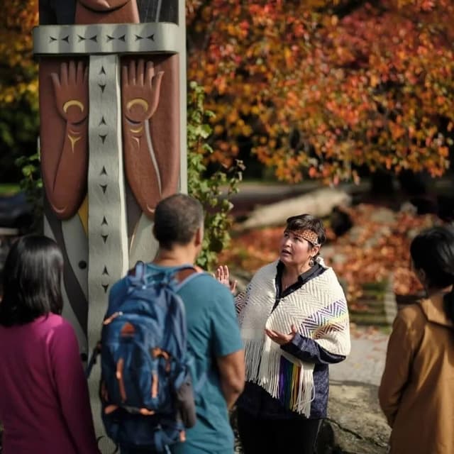 A Talaysay Tours guide talks with a small group beside a carved pole in autumn.
