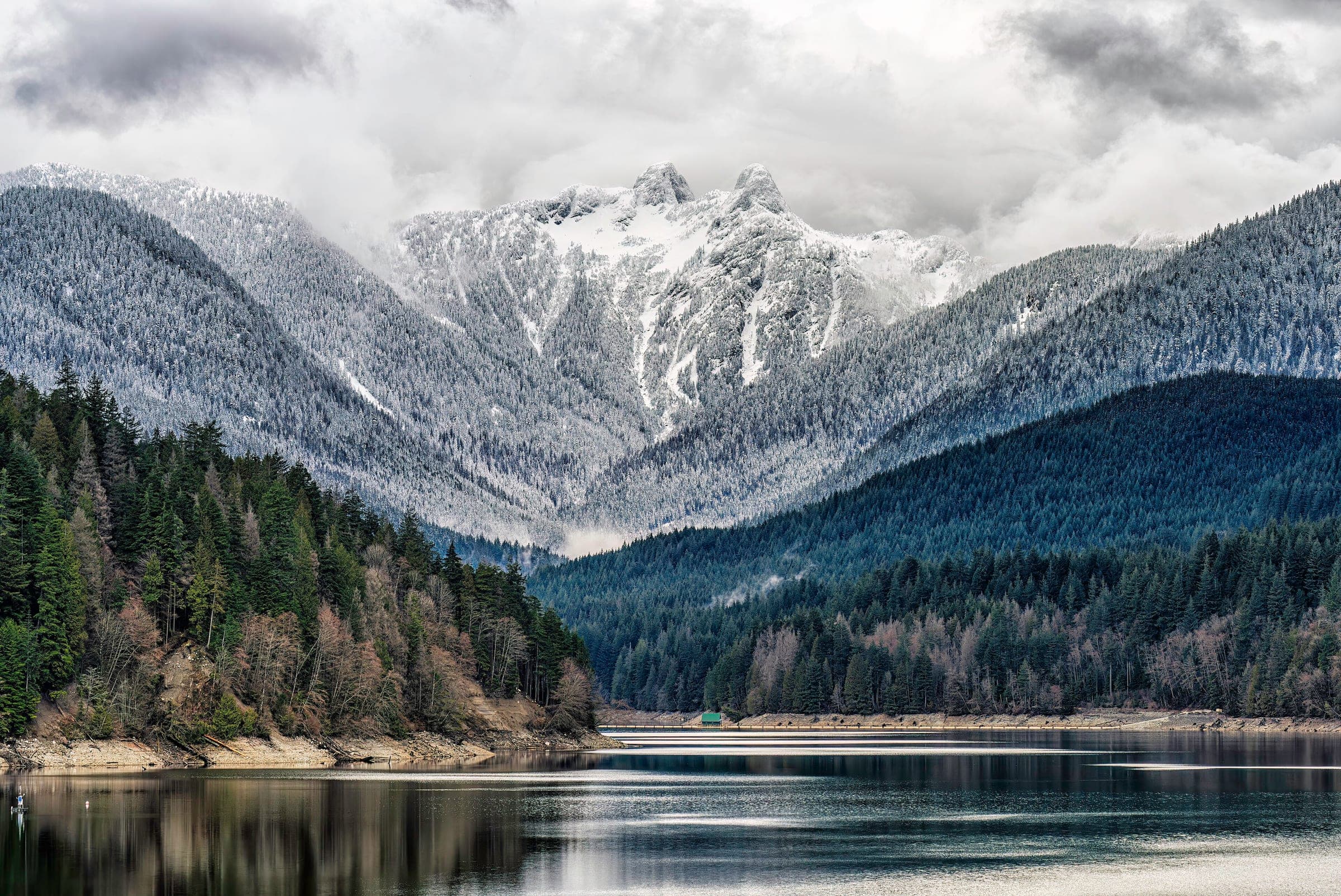 Snow dusts the forest and the twin peaks of the Lions above the still water of Capilano Lake.
