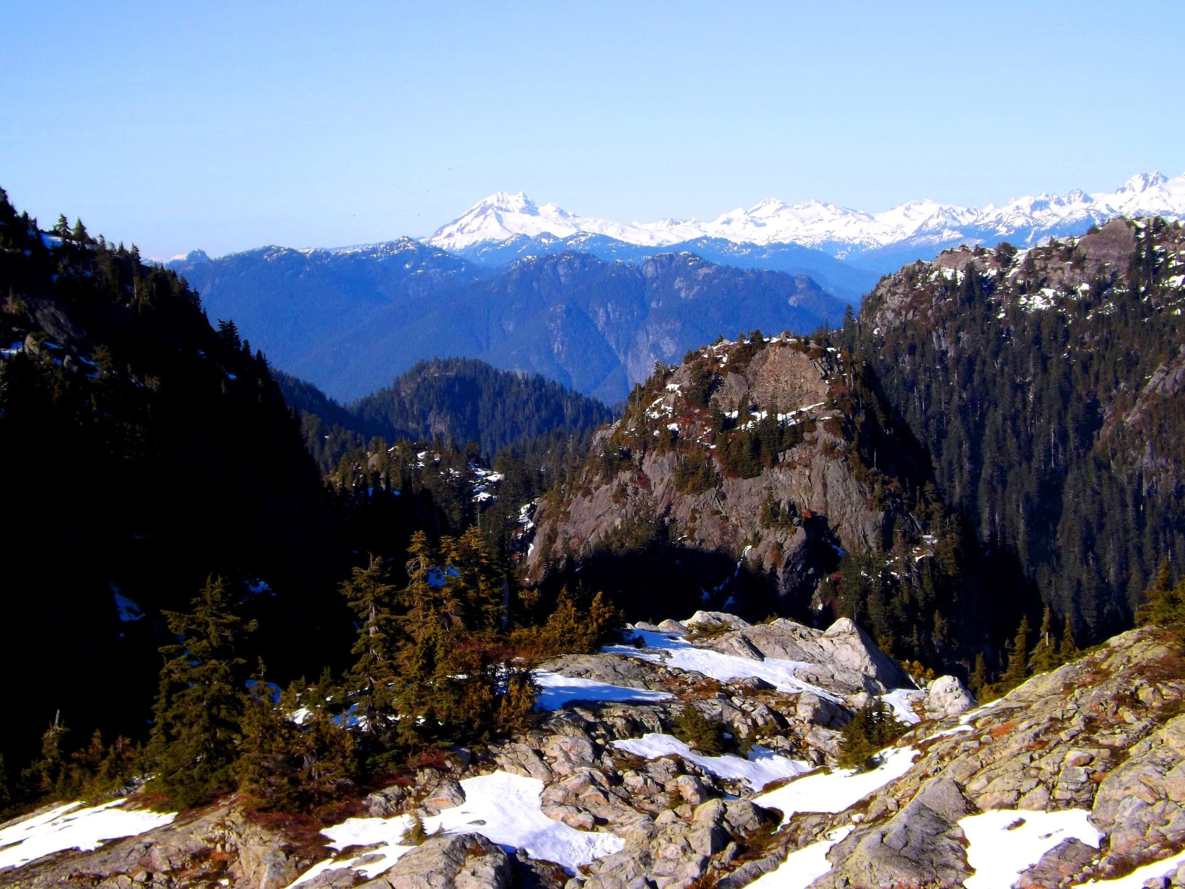 Patches of snow linger on the granite of Mount Seymour's alpine with white peaks across the valley.