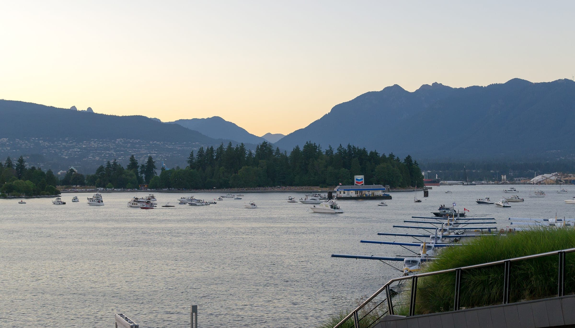 Boats rest on Coal Harbour at dusk below Stanley Park's trees and the North Shore mountains.