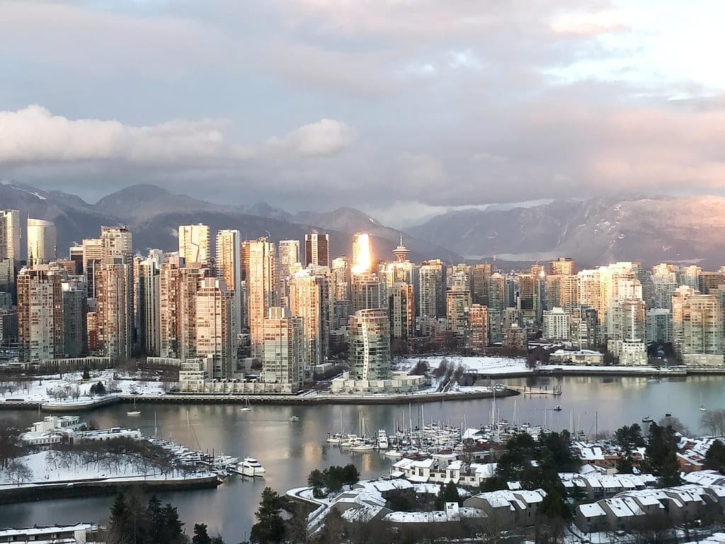 Low sun lights the downtown towers across False Creek as snow covers the roofs and docks in the foreground.