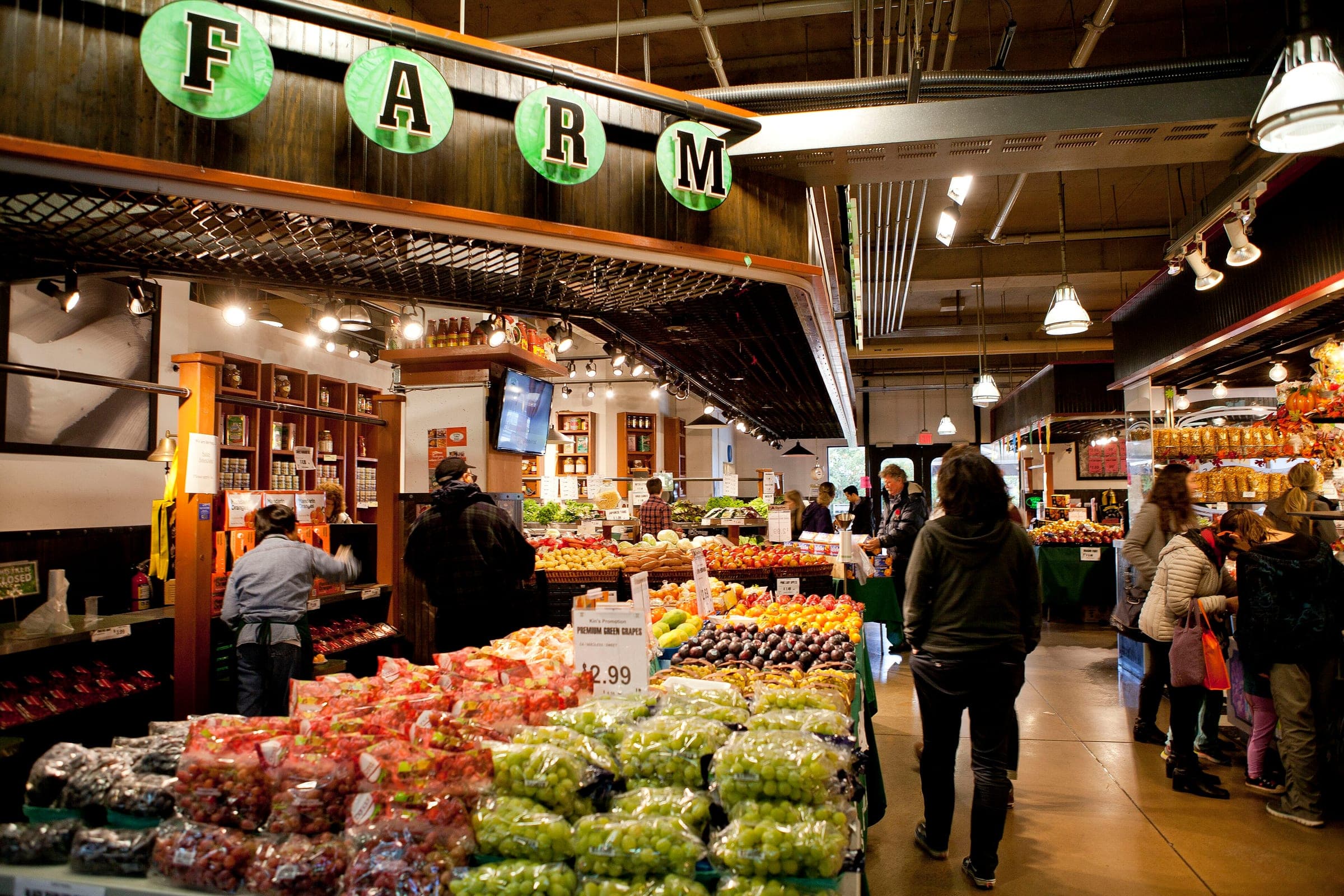 Shoppers browse the produce stall stacked with fruit and greens inside Lonsdale Quay Market.