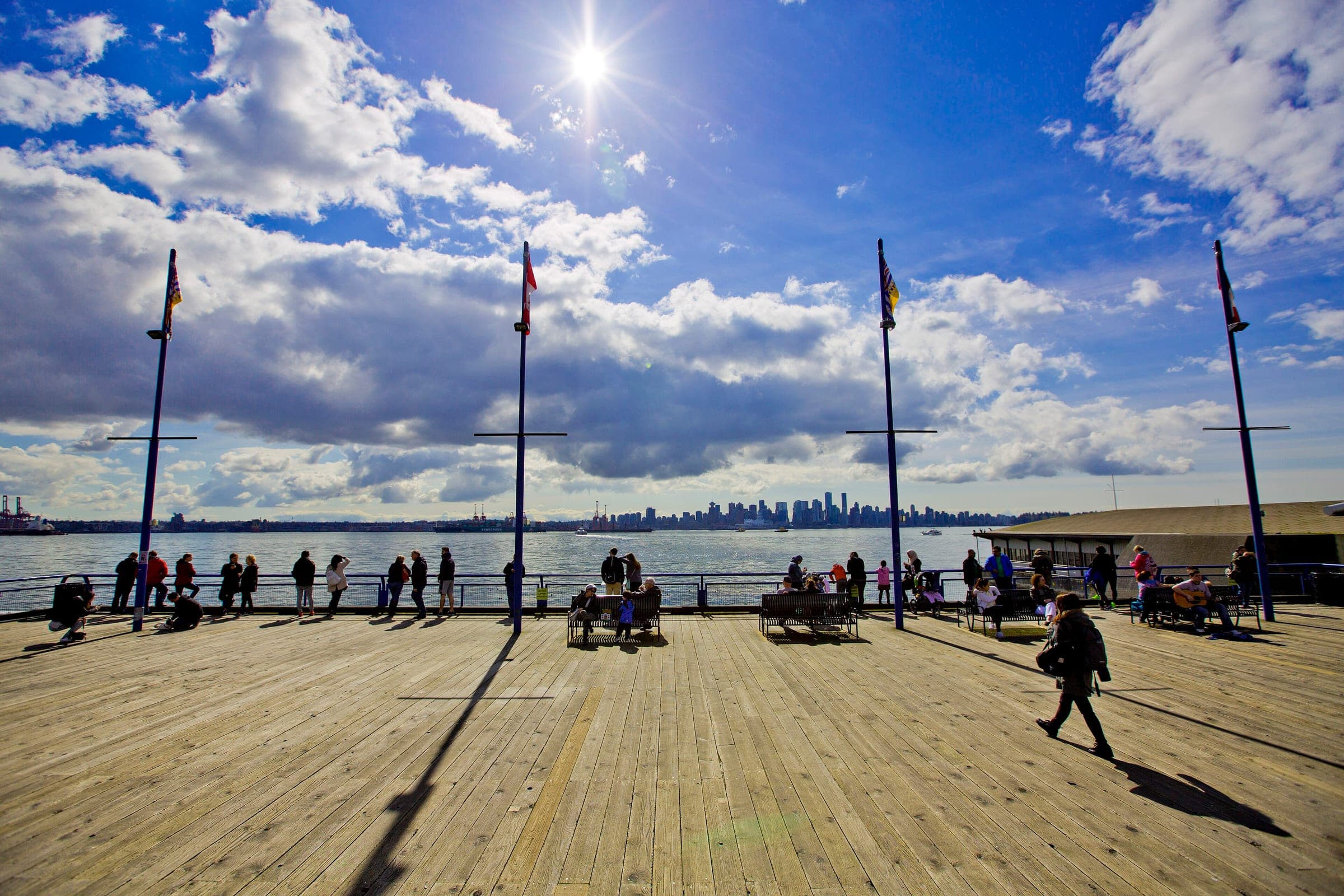Visitors walk the Lonsdale Quay pier as the sun lights the harbour and the downtown Vancouver skyline.