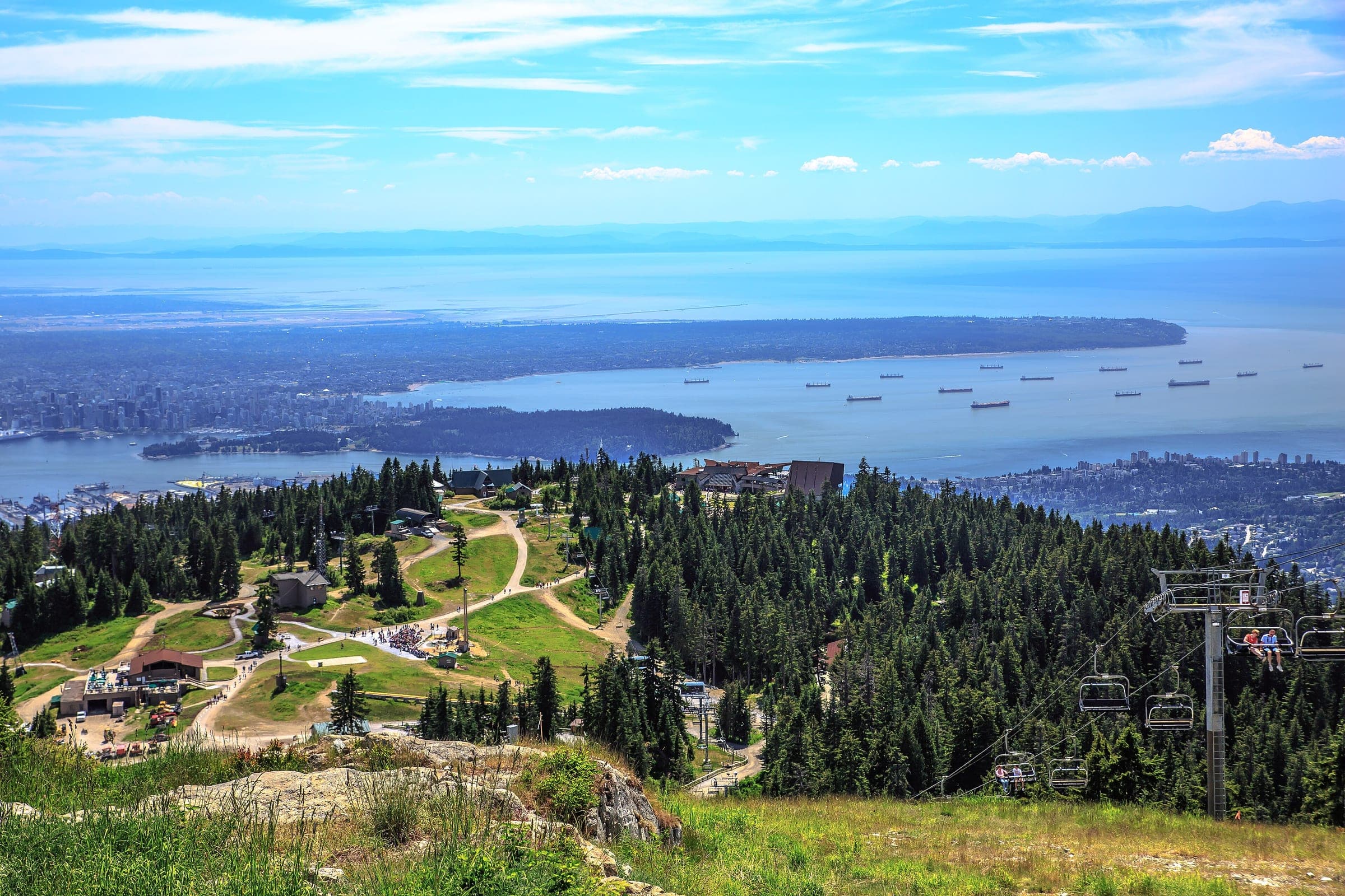 The Grouse Mountain ski area turns green in summer above Stanley Park, Burrard Inlet and the anchored freighters.