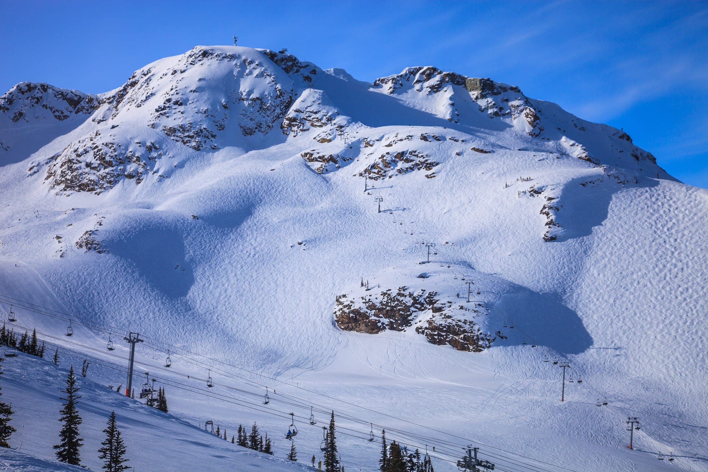Chairlifts climb a wide snowy alpine bowl below a rocky summit at Whistler Blackcomb.