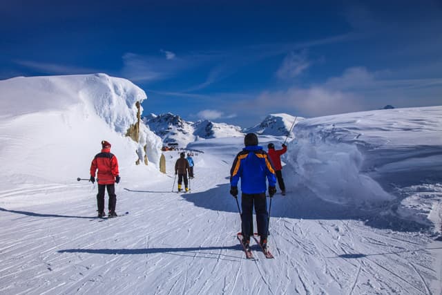 Skiers head along a groomed run between tall snowdrifts near the top of Whistler Mountain.