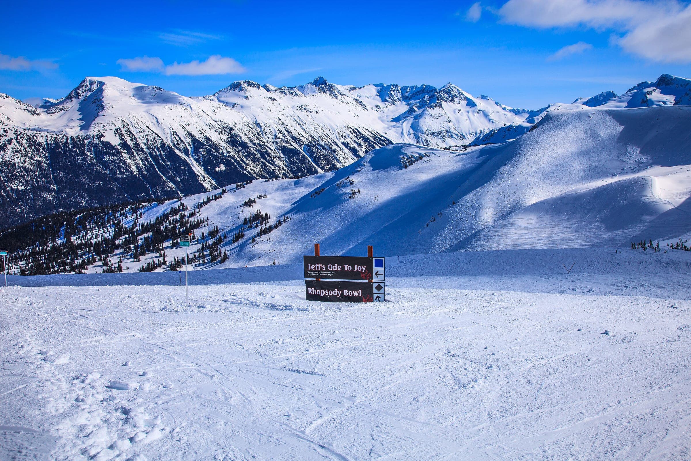 Signs for Rhapsody Bowl stand on Whistler Mountain's Symphony slopes below a row of snowy peaks.