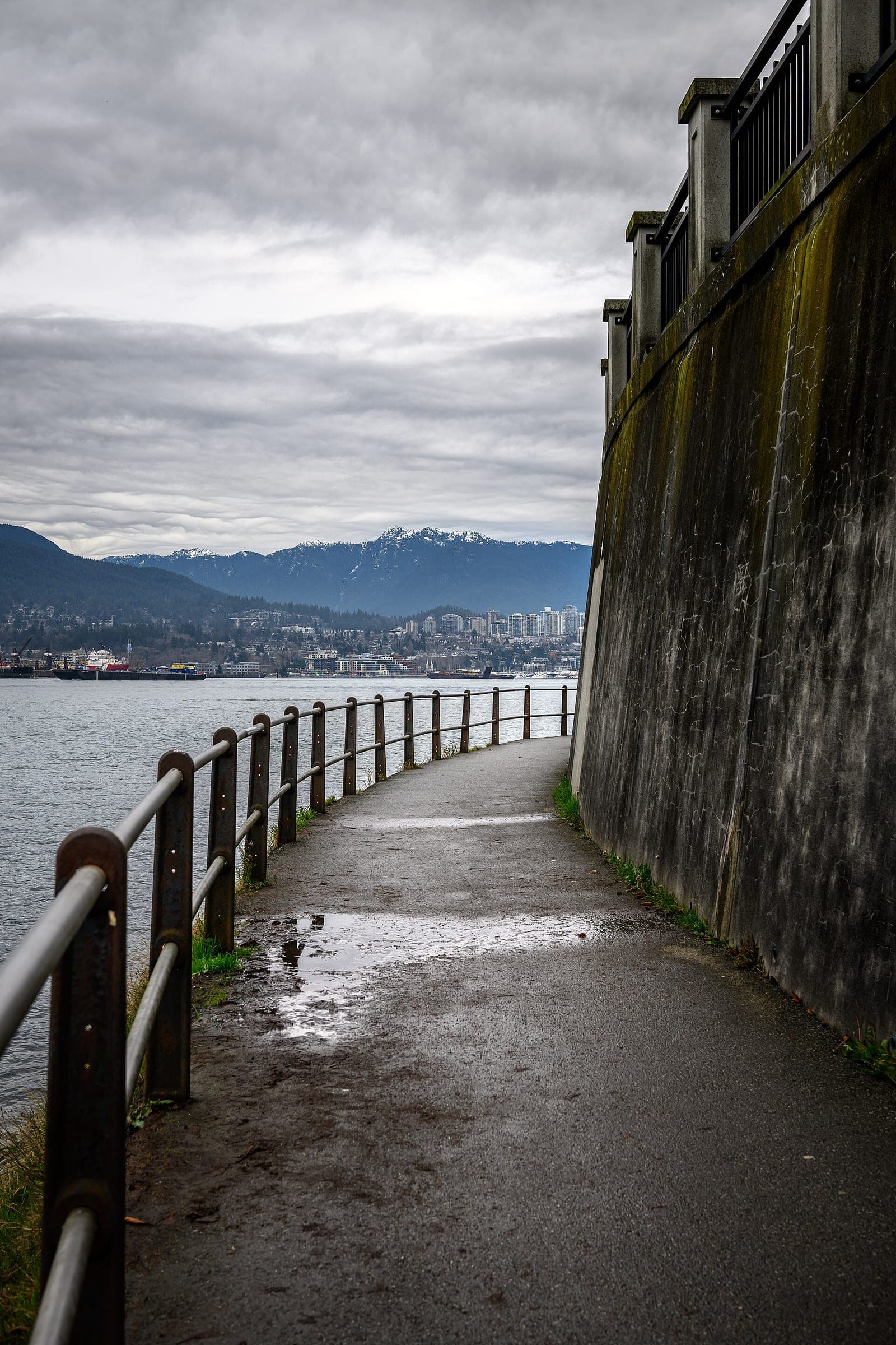 The wet Stanley Park Seawall curves along Burrard Inlet toward snowy North Shore peaks in December.