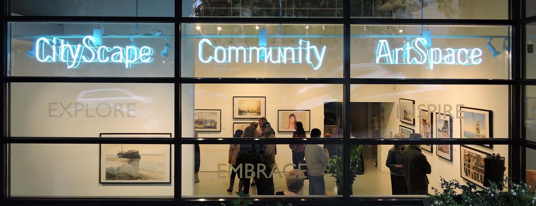 CityScape Community ArtSpace storefront windows lit up with visitors browsing framed art inside.