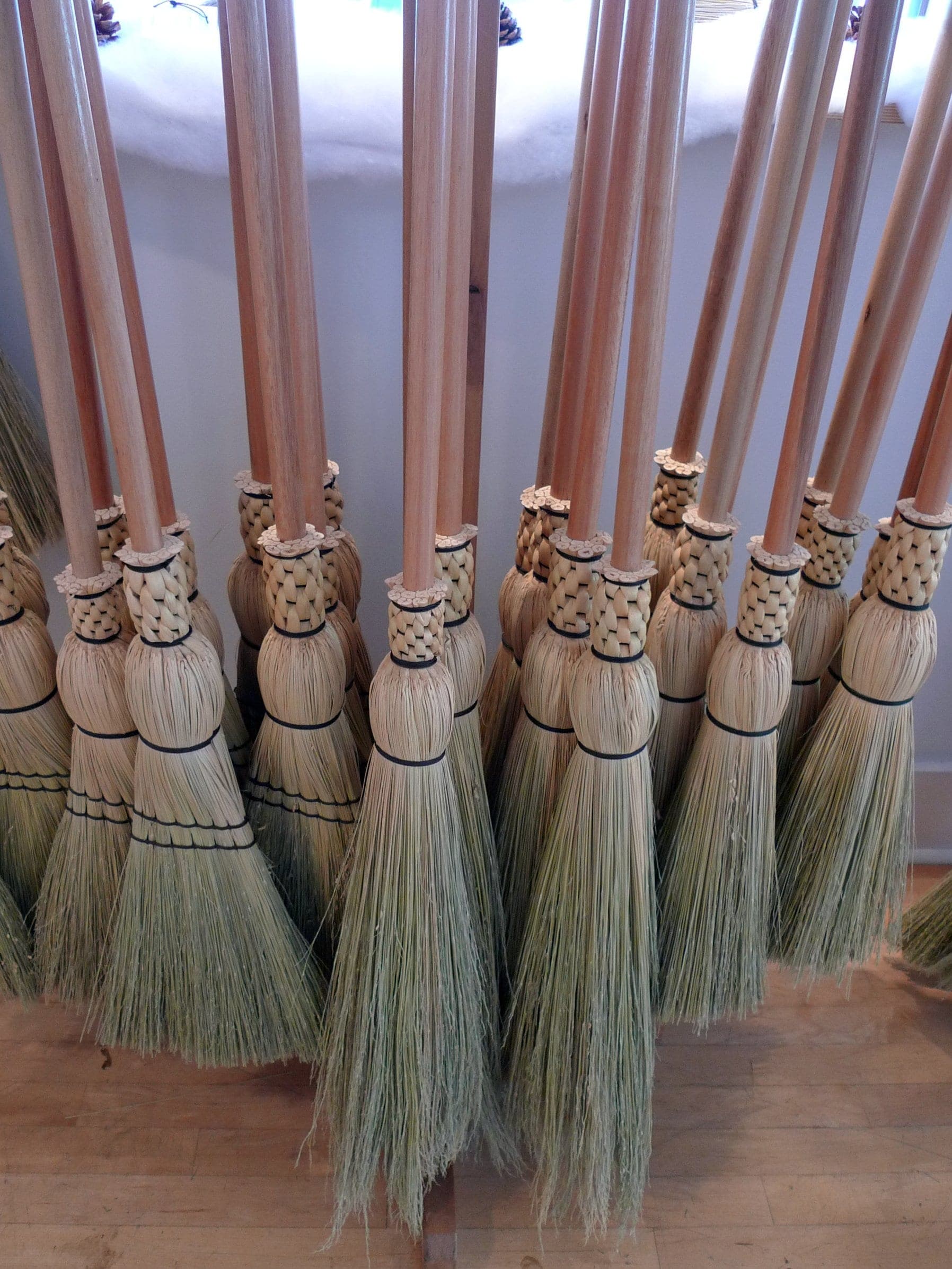 Hand-stitched brooms with natural wood handles stand together on the floor at Granville Island Broom Company.