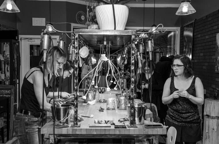 Two jewellers at the central workbench in the Juvelisto studio, with hanging lamps overhead.